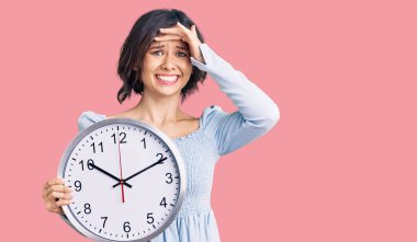 Elinde büyük bir saat tutan genç ve güzel bir kız. Elleri başının üstünde, şaşırmış ve sinirli bir yüz. 