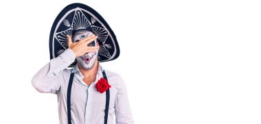 Arka planda ölü kostümü giymiş bir adam şok içinde yüzünü ve gözlerini kapayarak utanmış bir ifadeyle parmaklarının arasından bakıyor.. 