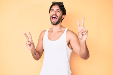 Yaz bakışı ve gülümseyen güneş gözlüğü takan yakışıklı İspanyol adam parmaklarını zafer işareti yaparken kameraya bakıyor. İki numara.. 