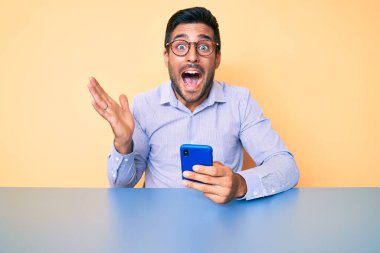 Genç İspanyol adam akıllı telefon kullanarak zaferi kutluyor. Gülümsüyor ve ellerini kaldırıyor. 