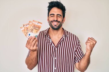 Avro banknotları tutan yakışıklı İspanyol adam gururla bağırıyor, zaferi ve başarıyı kutluyor. 