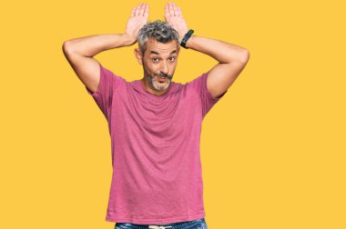 Orta yaşlı, gri saçlı, günlük kıyafetler giyen, tavşan kulağı yapan, avuç içi hareketleriyle kuşkucu ve şüpheci görünen bir adam. Paskalya tavşanı konsepti. 