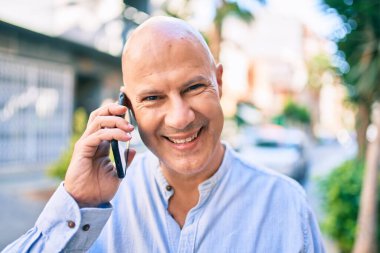 Orta yaşlı kel adam gülümsüyor. Şehirdeki akıllı telefondan mutlu mesut konuşuyor..