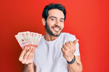 İspanyol asıllı genç adam elinde 10 Kolombiya pezosu ile gururla bağırıyor zaferi ve başarıyı kutluyor. 