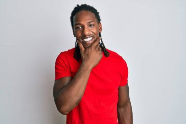 Saçları örgülü Afro-Amerikan bir adam kameraya kendinden emin bir şekilde bakıyor kollarını kavuşturmuş ve çenesini kaldırmış gülümsüyor. Olumlu düşünmek. 