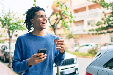 Genç Afrikalı Amerikalı adam şehrin caddesinde akıllı telefon kullanarak mutlu gülümsüyor..
