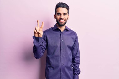 Sakallı, sıradan tişörtlü, genç ve yakışıklı bir adam iki numarayı gösterip, gülümseyerek kendinden emin ve mutlu görünüyor.. 