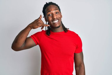 Saçları günlük kıyafetlerle örülü Afro-Amerikan bir adam gülümseyerek telefonla el ve parmak hareketleriyle telefonla konuşuyor. iletişim kavramları. 
