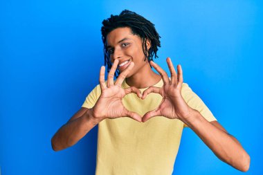 Genç Afro-Amerikalı sıradan kıyafetler giyen, aşık gülümseyen, elleriyle kalp sembolü yapan bir adam. romantik kavram. 