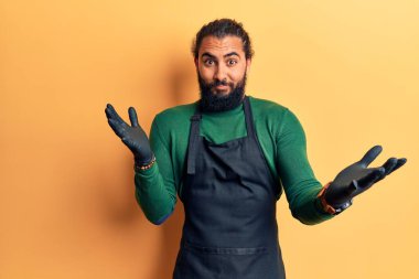 Berber önlüğü giyen genç bir Arap, elleri ve kolları havada, kafası karışmış bir ifade takınıyor. şüphe kavramı. 