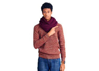 Genç, Afro-Amerikan bir adam günlük kışlık süveter ve atkı giymiş endişeli ve gergin bir şekilde işaret eden işaret parmağı, endişeli ve şaşırmış bir ifade. 