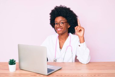 Doktor steteskobu giyen genç Afro-Amerikalı kadın bir fikir ya da soruyla şaşırmış bir şekilde bilgisayarla çalışıyor. 