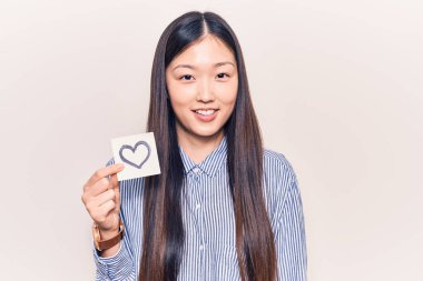 Genç, güzel Çinli bir kadın elinde kalp şeklinde bir hatırlatıcı taşıyor. Pozitif ve mutlu görünüyor. Kendine güvenen bir gülümsemeyle dişlerini gösteriyor. 
