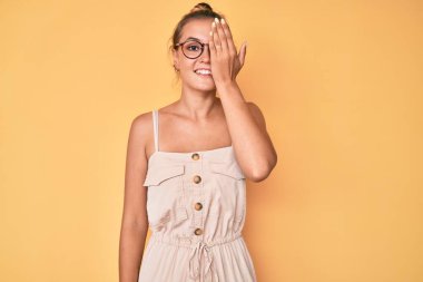 Yazlık elbise giyen güzel beyaz kadın bir gözünü eliyle kapatıyor, yüzünde kendine güvenen bir gülümseme ve sürpriz bir duygu var.. 