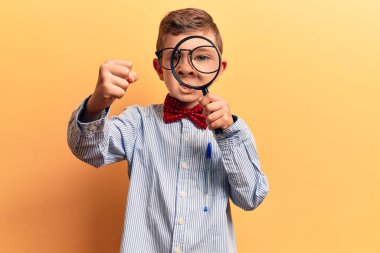 Sevimli sarışın çocuk inek papyonu takıyor ve elinde büyüteçle sinirlenmiş ve sinirlenmiş bir şekilde bağırıyor. Öfkeyle ve el kaldırarak deli gibi bağırıyor. 