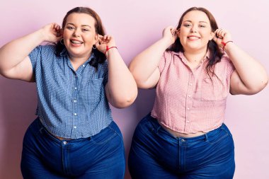 Genç ve cüsseli ikizler gülümseyerek parmaklarıyla kulaklarını çekiyorlar. Komik bir jest. deneme sorunu 