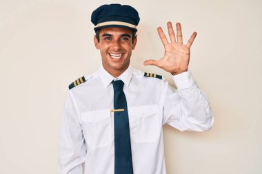 İspanyol asıllı genç adam uçak pilotu üniforması giyiyor. Beş numaralı parmaklarıyla işaret ediyor ve gülümsüyor. Kendinden emin ve mutlu.. 