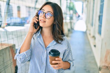 Ciddi bir suratı olan genç İspanyol iş kadını şehirdeki akıllı telefondan konuşuyor..