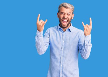 Zarif tişört giyen, çılgın bir ifadeyle bağıran genç, yakışıklı sarışın adam elleri havada rock sembolü yapıyor. Müzik yıldızı. ağır müzik konsepti. 