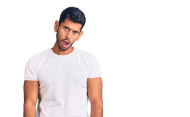 Şok olmuş gibi giyinen genç Latin adam şüpheci ve alaycı görünüyor, ağzı açık kalınca şaşırıyor. 