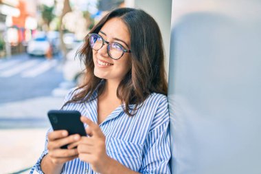 Genç İspanyol iş kadını şehirde akıllı telefon kullanarak mutlu gülümsüyor..