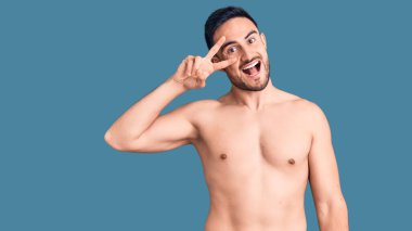 Mayo giyen genç yakışıklı adam barış sembolü yapıyor. Yüzünde parmaklar, gülümseyerek zaferi gösteriyor. 