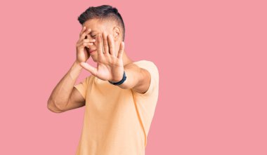 Genç, yakışıklı, günlük kıyafetler giyen, elleriyle gözleri kapatan, üzgün ve korku ifadeleriyle jestler yapan bir adam. utangaç ve olumsuz kavram. 