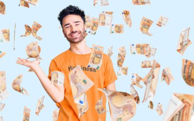 Üzerinde mutluluk mesajı olan tişört giyen genç İspanyol adam mutlu bir şekilde sunum yapıyor ve avuç içi kameraya bakıyor..