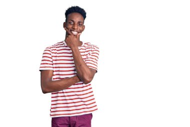 Sıradan kıyafetler giyen genç Afro-Amerikalı adam kameraya kendinden emin bakıyor kollarını kavuşturmuş ve çenesini kaldırmış gülümsüyor. Olumlu düşünmek. 