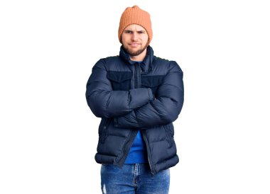 Kışlık kıyafetler giyen, kuşkucu ve gergin genç bir adam. Yüzünde çapraz kollarla onaylamayan bir ifade var. negatif kişi. 