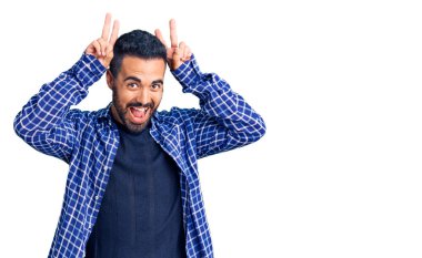 Genç İspanyol bir adam günlük kıyafetler giyiyor komik ve çılgın poz veriyor parmakları tavşan kulağı gibi, neşeli gülümsüyor 