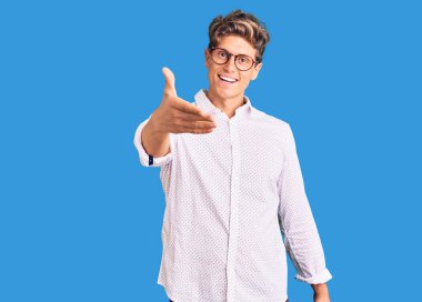 İş kıyafetleri ve gözlük takan yakışıklı genç adam dostça bir selamlama ve hoş geldin hediyesi olarak tokalaşıyor. başarılı iş. 