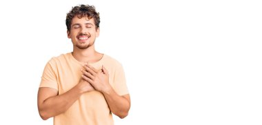 Kıvırcık saçlı, sıradan kıyafetler giyen, göğsünde elleri kapalı, yüzünde minnet ifadesi olan genç yakışıklı bir adam. sağlık kavramı. 