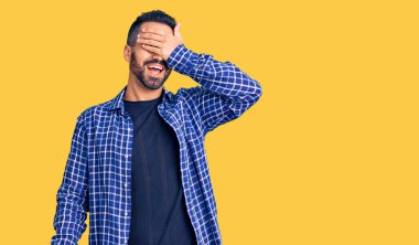 Gündelik kıyafetler giyen, gülümseyen ve gülümseyen genç İspanyol adam şaşırmak için gözlerini kapatıyor. kör kavram. 