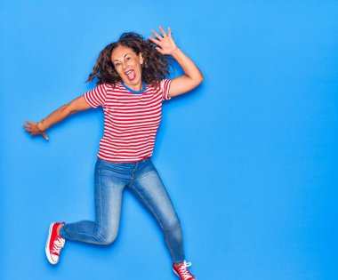 Orta yaşlı, güzel, İspanyol bir kadın. Günlük kıyafetler giyip mutlu gülümsüyor. İzole edilmiş mavi arka planda yüzünde gülümsemeyle zıplıyor