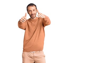 Gündelik giysiler giyen genç bir adam elinle olumlu jest yapıyor, gülümsüyor ve başarı için seviniyor. kazanan jest. 