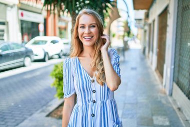 Sarışın, güzel, beyaz bir kadın. Güneşli bir günde gülümsüyor ve neşeli yürüyor.