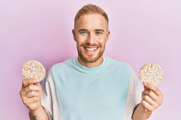 Homem Caucasiano Jovem Comendo Biscoitos Arroz Saudáveis Sorrindo Com Sorriso — Fotografia de Stock