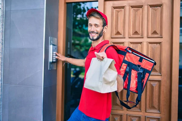 Caucasian delivery man wearing red uniform and delivery backpack smilly happy outdoors holding paper bag
