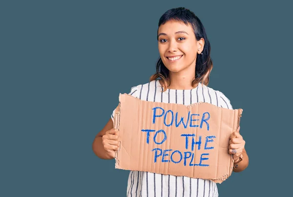 Young woman holding power to the people banner looking positive and happy standing and smiling with a confident smile showing teeth