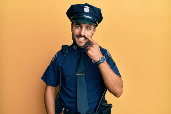 Handsome hispanic man wearing police uniform pointing with hand finger to face and nose, smiling cheerful. beauty concept