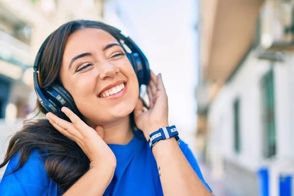 若いヒスパニック系の女性が街を歩くヘッドフォンを使用して音楽を聞いて幸せな笑顔 — ストック写真