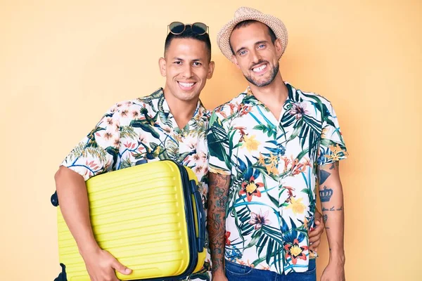 Genç eşcinsel iki adam ellerinde bavullarıyla yaz tatiline çıkıyorlar. Olumlu ve mutlu görünüyorlar. Dişlerini gösteren bir gülümsemeyle duruyorlar. 