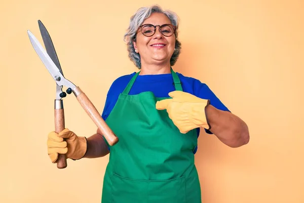 Ältere Hispanische Frau Trägt Gärtnerschürze Und Handschuhe Und Zeigt Mit — Stockfoto