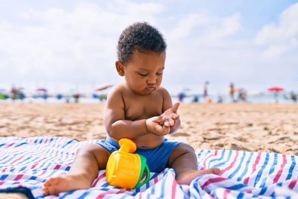 愛らしいアフリカ系アメリカ人の幼児はおもちゃで遊んでいます砂の上に座ってビーチ — ストック写真