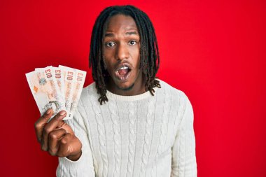 Elinde 10 sterlinlik saç örgüsü olan Afro-Amerikan bir adam. Banknotlar. Şaşırtıcı bir şekilde ağzı açık ve korkmuş. 