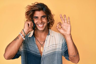 Genç İspanyol adam akıllı telefonda konuşuyor parmaklarıyla imza atıyor, gülümsüyor ve mükemmel bir sembol oluşturuyor. 