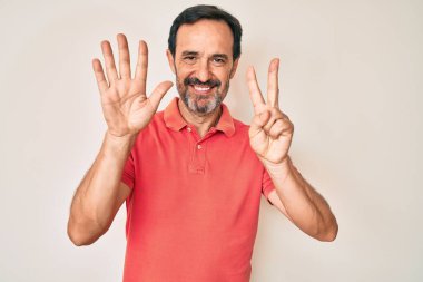 Orta yaşlı İspanyol bir adam gündelik kıyafetler giyer ve yedi numaralı parmaklarını göstererek gülümseyerek mutlu ve kendinden emin bir şekilde gösterir.. 