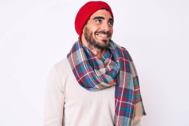 Kış süveteri, eşarp ve yün şapka giyen kıvırcık saçlı, yakışıklı genç adam, rahat profil pozu, doğal bir yüz ve kendine güvenen bir gülümseme.. 