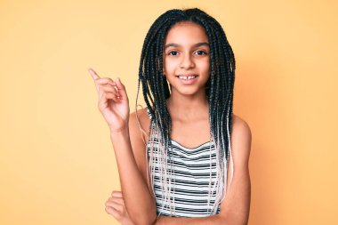 Sarı arka planı örgü örmüş, mutlu gülümseyen, el ve parmak uçlarını gösteren Afro-Amerikan kızı. 